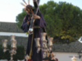 Estatua de Jesús crucificado en un paso procesional, rodeado por flores y acompañado de otros participantes.