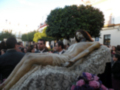 Una escultura de Jesucristo en una procesión religiosa, rodeada por personas y flores.