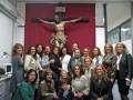 Un grupo de personas posa para una foto en un entorno religioso, con una figura del Cristo crucificado en el fondo.