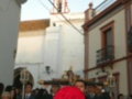 Fotografía de una procesión religiosa en un entorno urbano, con personas vestidas formalmente y portando una imagen de Cristo. La escena se desarrolla en un entorno histórico con edificios antiguos y una iglesia visible al fondo.