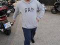 Un hombre camina por una calle con motocicletas y coches en el fondo. Viste un sudadera de GAP con pantalones azules.