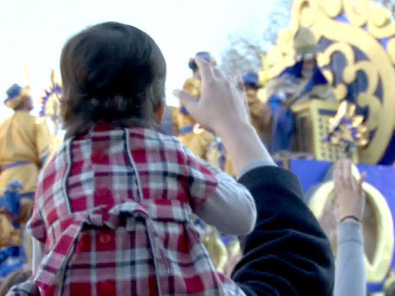 Niña disfrutando de un desfile festivo, capturando momentos con su teléfono móvil.
