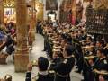 Banda de música en uniforme desfilando en una iglesia, con instrumentos y vestimenta tradicional.
