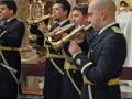 Cuatro músicos militares tocan instrumentos en una iglesia, con un altar dorado y estatuas religiosas al fondo.