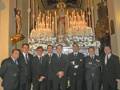 Un grupo de hombres en trajes formales posa frente a un altar ornamental en una iglesia.