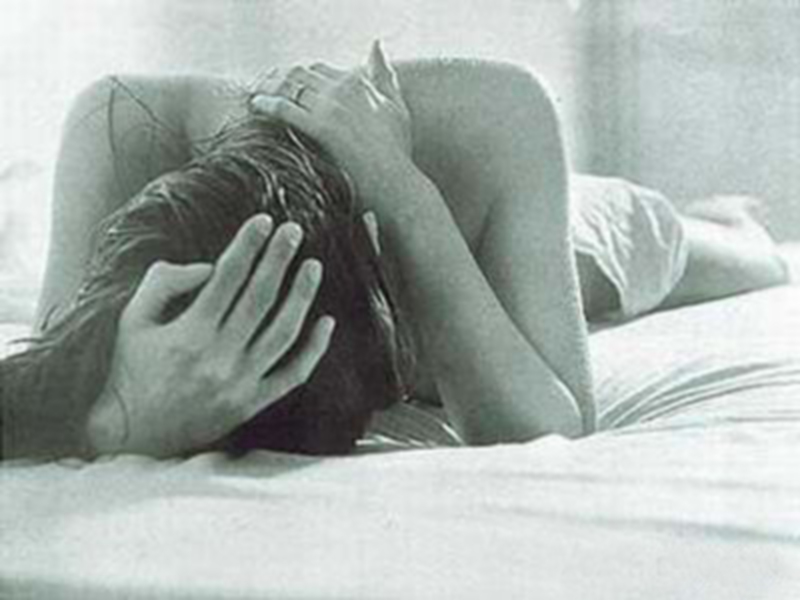 Una persona acostada en la cama con las manos sobre su cabeza, expresando una sensación de angustia o tristeza.