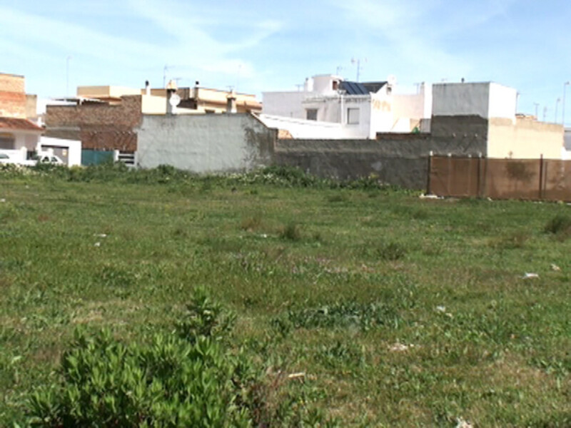 Terreno vacío con casas y techos en el fondo bajo un cielo azul claro.