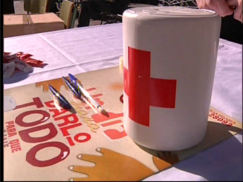Una taza con un símbolo cruzado rojo en blanco, posiblemente de la Cruz Roja, sobre una mesa con un cartel que dice "PARA TODO".