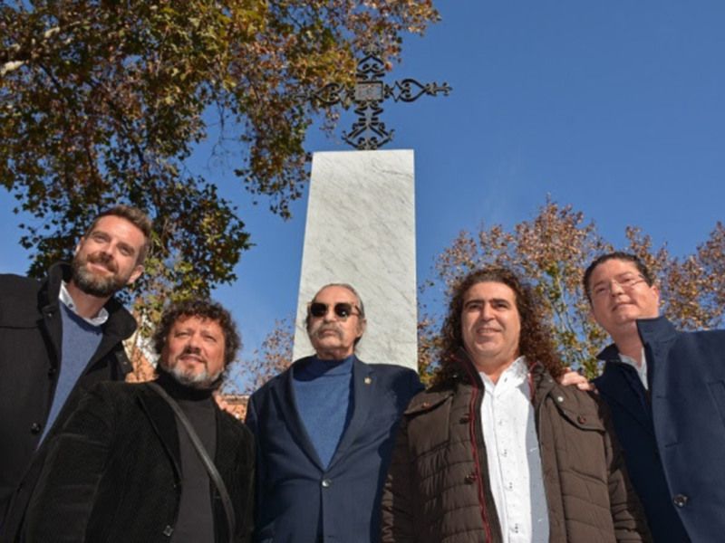 Grupo de hombres posando en frente de una cruz y un monumento en un día soleado.