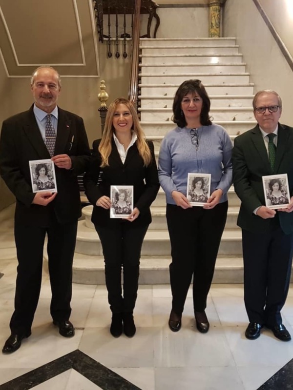 Fotografía de cuatro personas posando con fotos en manos, frente a una escalera de mármol.