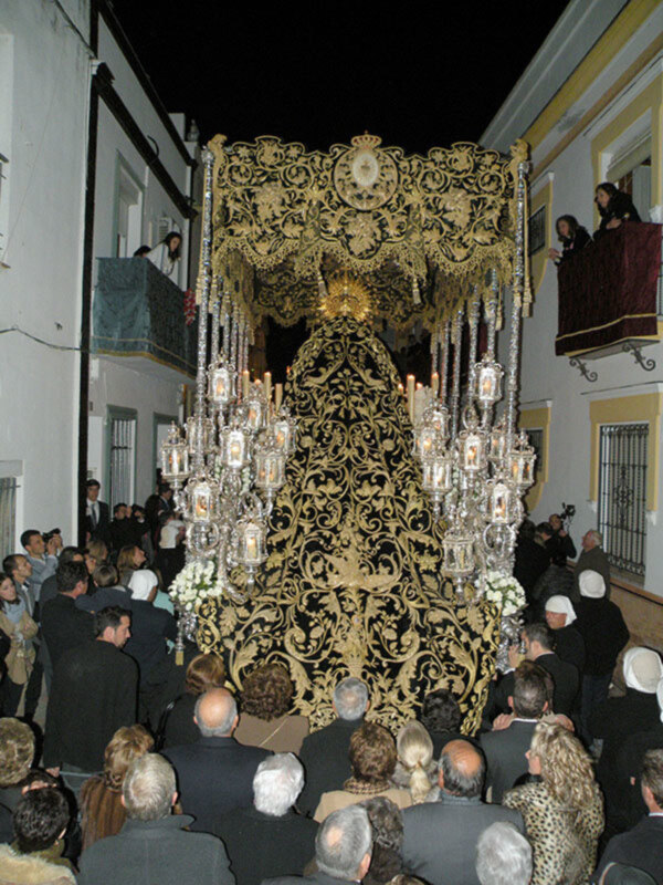 Procession of a religious figure draped in ornate, golden fabric, with people gathered around and taking photos.