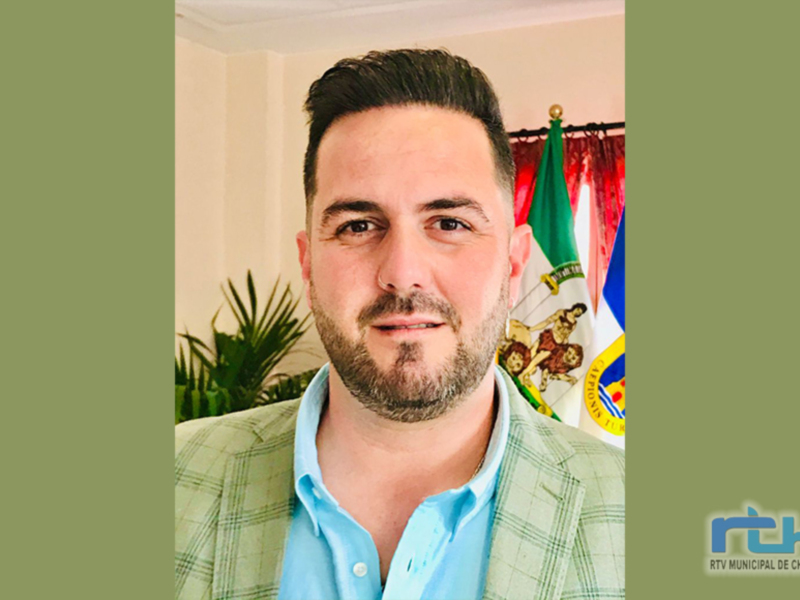 Retrato de hombre con traje y bandera de Chipiona en el fondo.