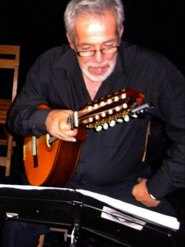 Músico toca una guitarra clásica en un escenario oscuro.