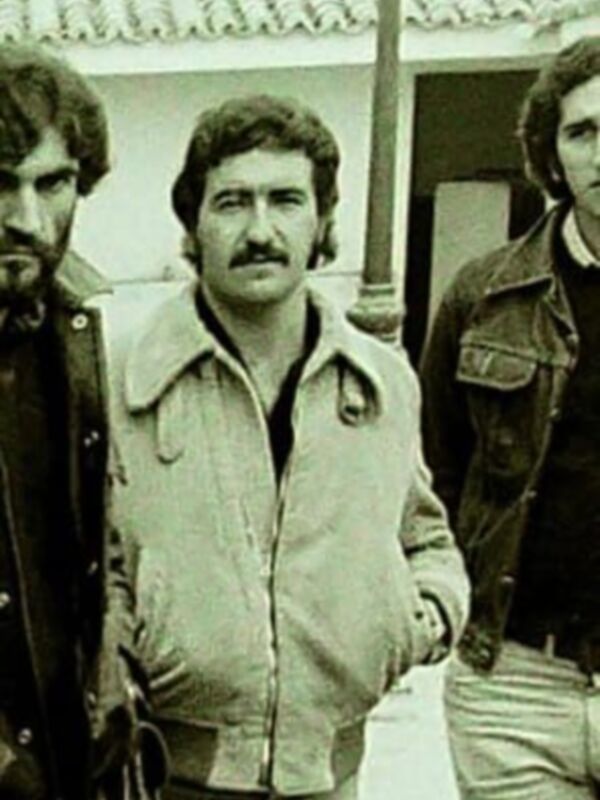 Tres hombres de los años 70 posando juntos al aire libre, con ropa de estilo retro y una lámpara de calle en el fondo.