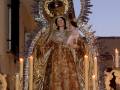 Procesión religiosa con imagen de la Virgen María adornada con velo y corona, rodeada de velas y ornamentos dorados.