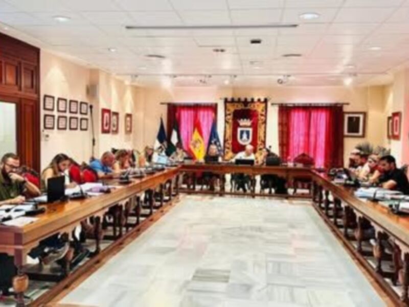 Reunión en un salón de conferencias con participantes sentados alrededor de una larga mesa, discutiendo en un ambiente formal.