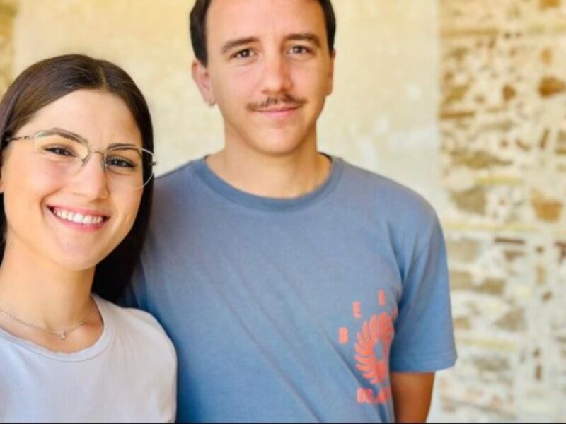 Dos personas sonrientes posan juntas frente a un muro de piedra.