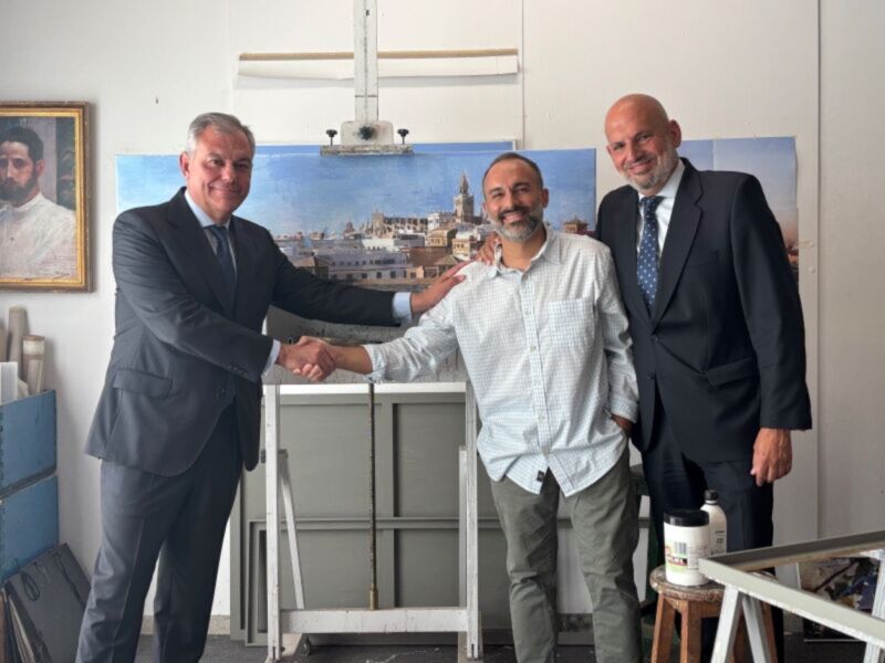 Tres hombres en trajes de negocios están apretando las manos, uno de ellos sonríe mientras el otro mira hacia la cámara. En el fondo hay una pintura que muestra un paisaje urbano con edificios y una iglesia. La escena se desarrolla en un entorno de oficina con muebles blancos y una pared decorada.