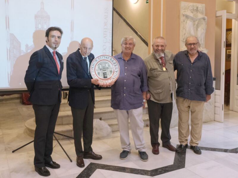 Una imagen de cinco hombres posando en una sala con un escudo en el centro. El ambiente es formal, probablemente en un evento o ceremonia oficial.
