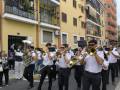 Músicos tocando instrumentos de viento en una calle con edificios amarillos y rojos.