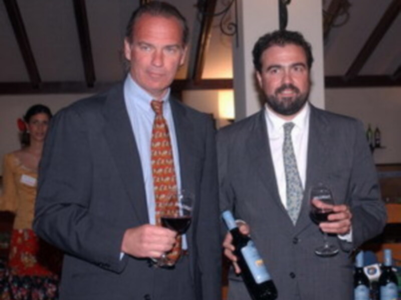 Dos hombres en traje disfrutan de una copa de vino en un ambiente social.