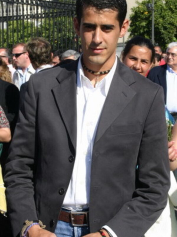Un hombre con una chaqueta de negocios, una camisa blanca y una correa de cuero en la cintura, posando para la foto.