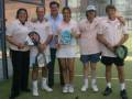 Grupo de personas posando en una cancha de tenis, con raquetas y pelotas.
