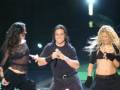 Tres personas en un escenario, dos hombres y una mujer, están cantando o actuando. La imagen parece ser de un concierto o evento musical.
