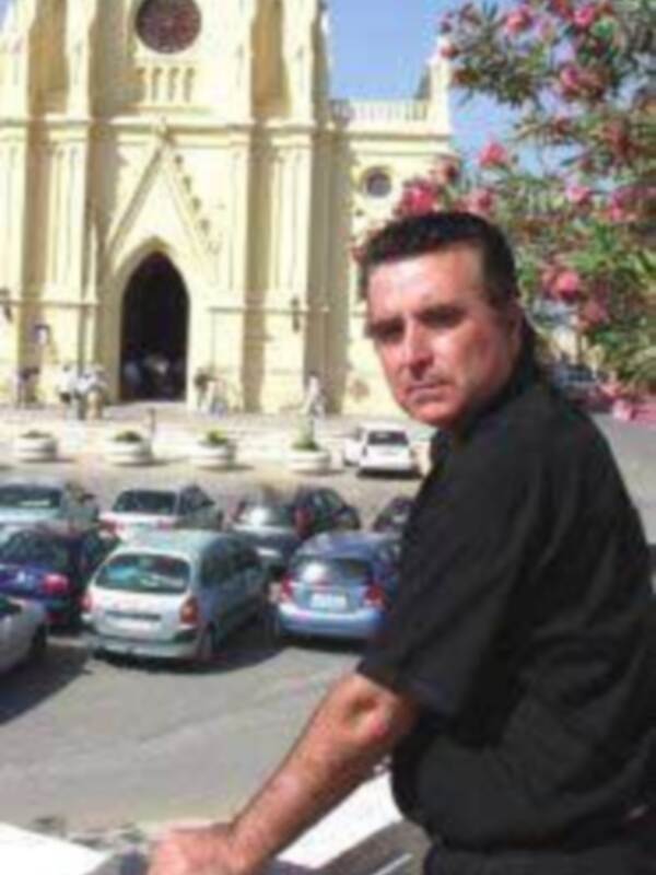 Persona frente a una iglesia con flores de olivo en el fondo.