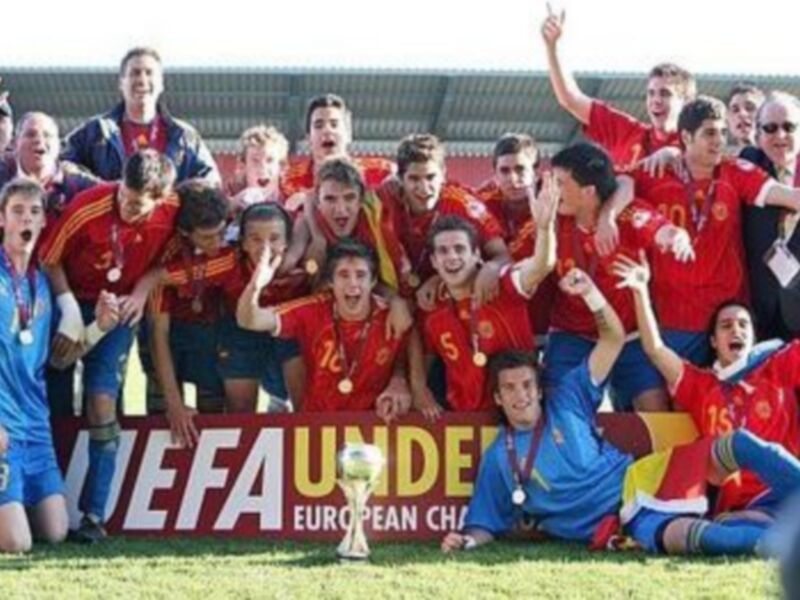 Jóvenes jugadores celebrando con medallas y banderas, en un campo de fútbol.