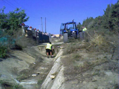 Trabajadores en una obra de construcción en una pendiente, con un tractor en el fondo y un canal de agua en el suelo.