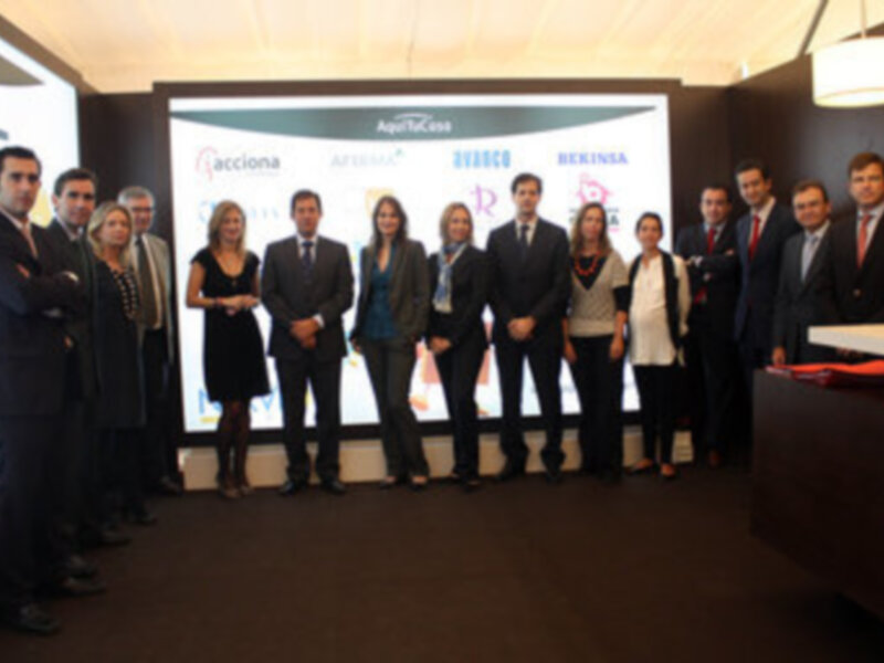 Equipo de profesionales en una presentación de negocios, con un fondo de pantallas de proyección en el fondo. Los miembros del equipo están vestidos formalmente, con chaquetas y corbatas. La imagen transmite un ambiente de negocios y profesionalismo.