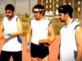Tres jóvenes en una cancha de atletismo, con un entrenador en el centro. Todos están vestidos con camisetas blancas y pantalones cortos, listos para el entrenamiento.
