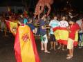 Un grupo de personas celebrando con banderas españolas y un payaso gigante en la noche.