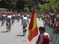 Corredores en bicicleta durante una carrera ciclista con un hombre en silla de ruedas portando la bandera española.