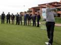 Un hombre golpea un palo de golf mientras otros observan en una pista de golf.