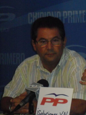 Un hombre con gafas habla en una conferencia de prensa frente a un fondo azul con el logo del PP. En la mesa hay una placa que dice "¡Soluciones YA!".