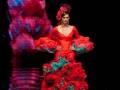 Una modelo vestida con un traje de flamenca rojo y verde, posando frente a una pantalla que refleja su imagen.