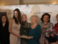 Una mujer sostiene un premio mientras otros individuos la observan en una ceremonia de reconocimiento.