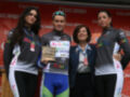 Ciclista en el podio con trofeo, acompañado de dos mujeres y una señora en traje oficial, ante fondo de Cruzcampo.