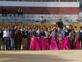 Grupo de jóvenes y adultos posando en un ruedo de toros con trajes de flamenca y trajes típicos, en un evento tradicional.