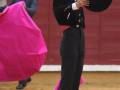 Un torero en traje negro y sombrero, con una capa rosa, preparándose para el toreo.