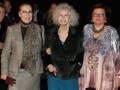 Tres mujeres mayores caminan juntas, una con abrigo beige y chaqueta de leopardo, otra en negro brillante y la tercera con vestido estampado.