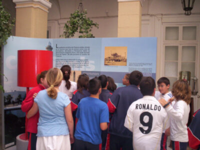 Niños observando una exposición histórica en un museo, con una imagen de la Torre de Capón en el fondo.