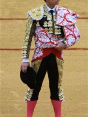 Un torero en uniforme tradicional, con un chaleco rojo y blanco, una chaqueta dorada con detalles dorados y guantes negros.