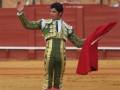 Un torero en traje de luces y capa roja se prepara para entrar al ruedo durante una corrida de toros.