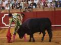 Un torero con capa y espada enfrenta a un toro negro en la plaza de toros. La audiencia observa atentamente desde el fondo, mientras el torero prepara su próximo movimiento.