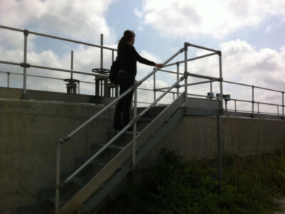 Una persona subiendo una escalera metálica en un entorno industrial, con un cielo nublado de fondo.