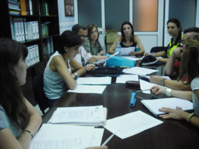 Una reunión de trabajo en un despacho con personas sentadas alrededor de una mesa, mostrando documentos y equipos.