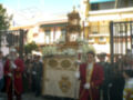 Procesión religiosa con estandarte dorado y vestimenta tradicional en una calle urbana.